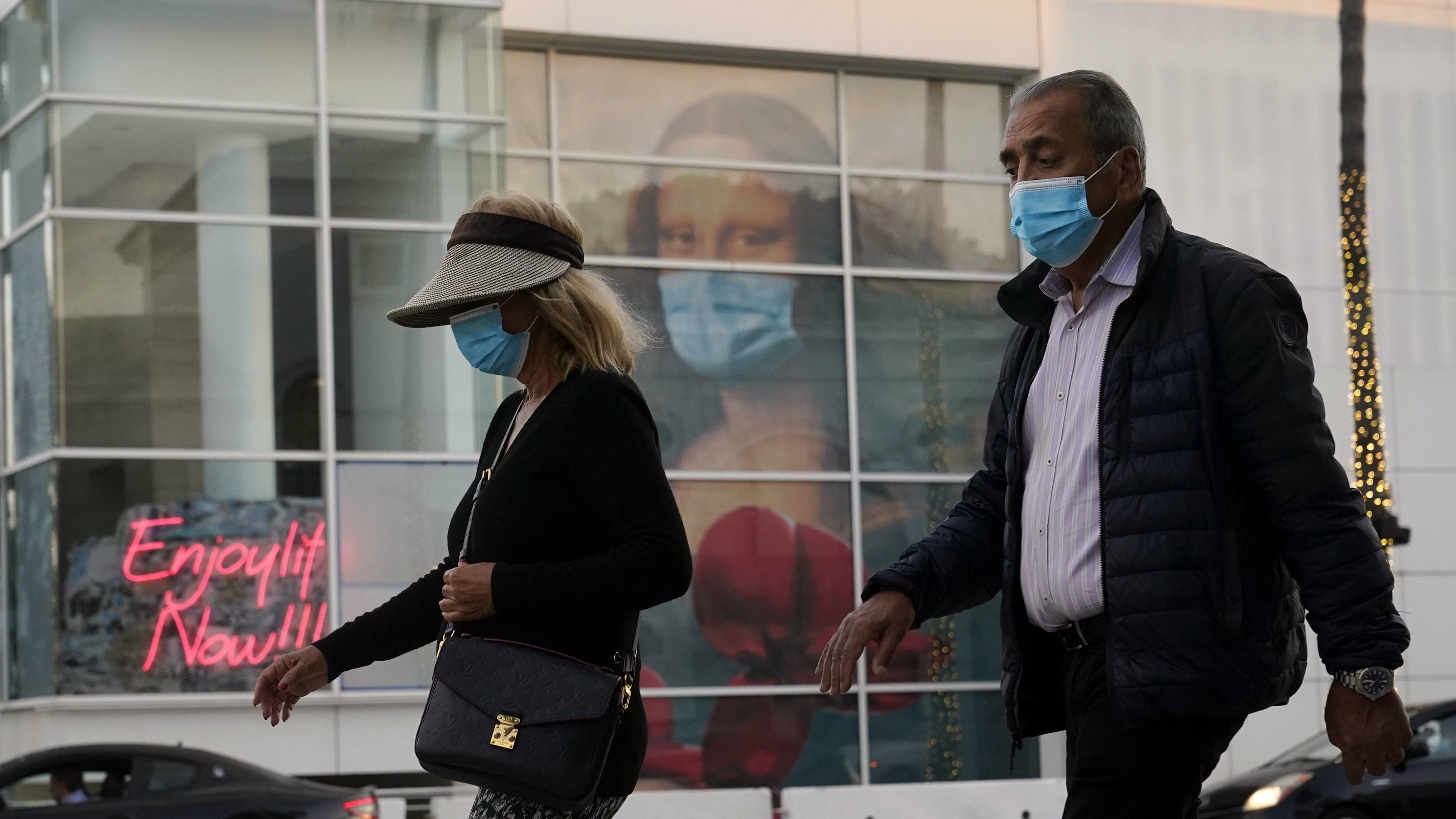 Masked pedestrians walk past of a COVID 19-themed mural depicting Leonardo da Vinci's Mona Lisa on  Dec. 9, 2020, in Beverly Hills, Calif. (AP Photo/Marcio Jose Sanchez)